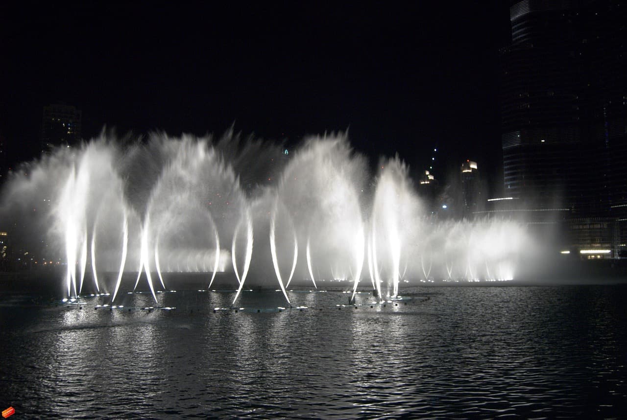 A wide choreographed fountain at night, illuminated jets arcing over dark water